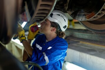 Frau mit Schutzhelm schaut sich Bremsscheiben eines Zug an.
