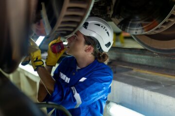Frau mit Schutzhelm schaut sich Bremsscheiben eines Zug an.