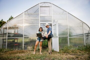 Zwei Personen arbeiten mit einem Laptop außerhalb des Gewächshauses